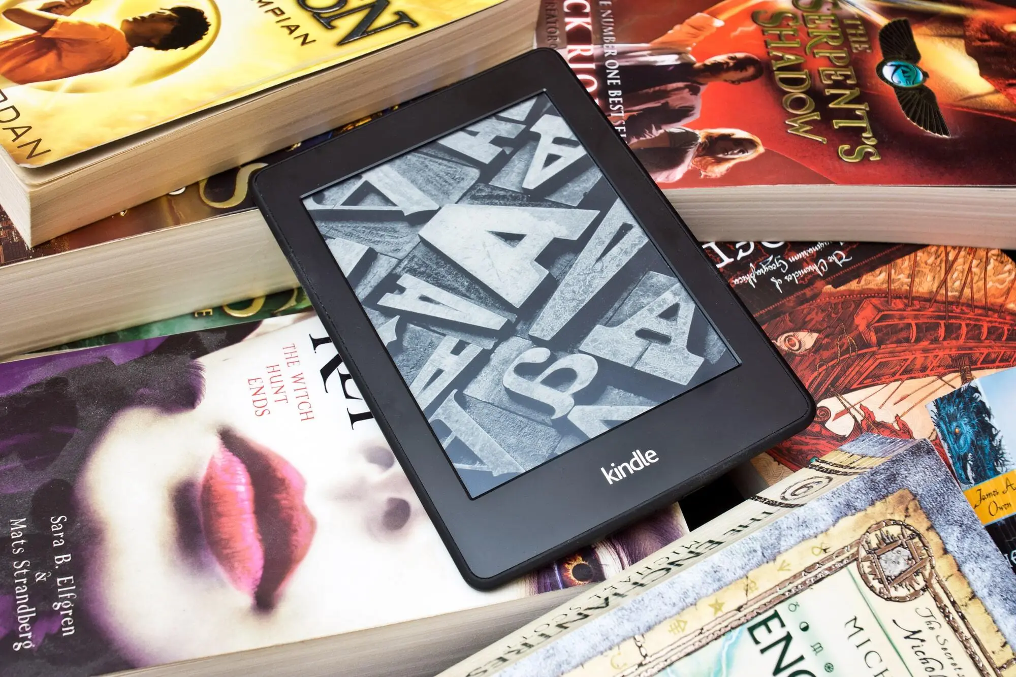 Kindle com livros ao fundo